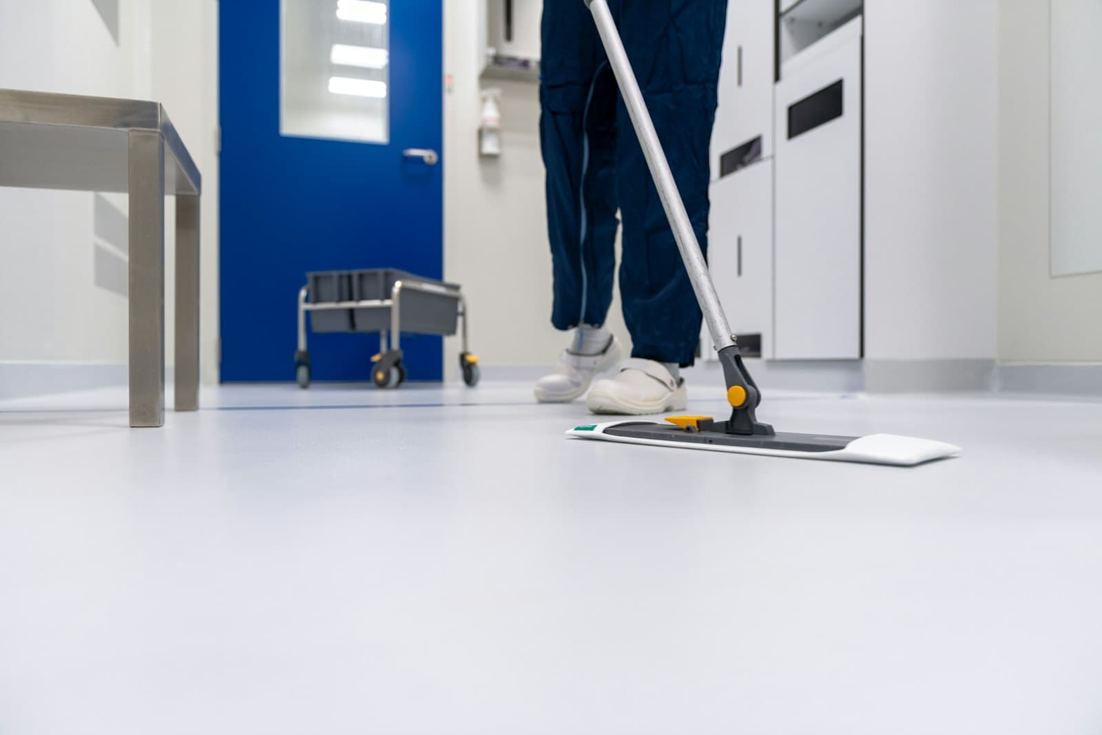 Cleaner in uniform mopping a bright white office corridor